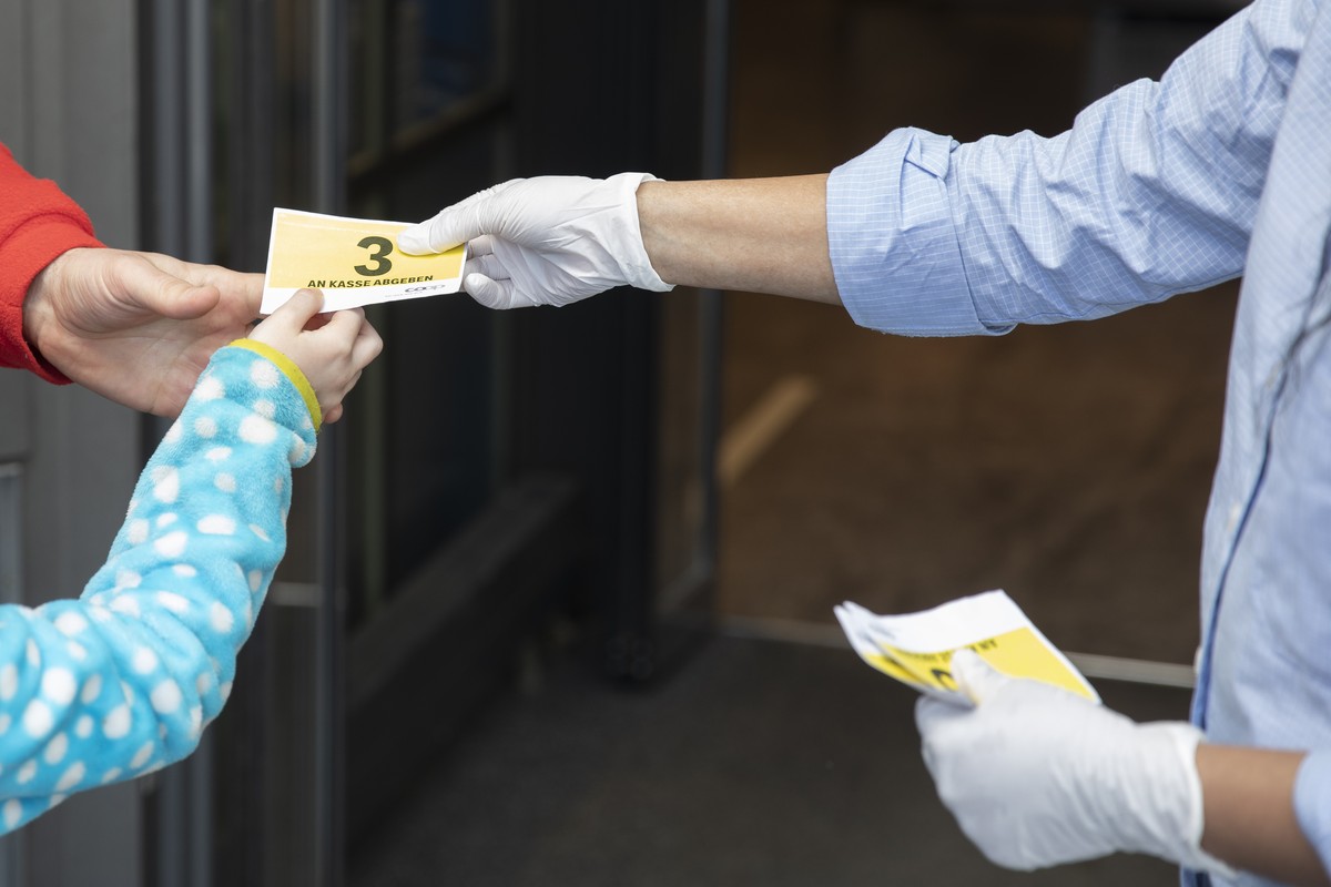 Eine Coop Mitarbeiterin uebergibt 2 Kunden Karten, damit die anwesenden Kunden im Geschaeft gezaehlt werden koennen, am Donnerstag, 19. Maerz 2020 in Bern. (KEYSTONE/Peter Klaunzer)