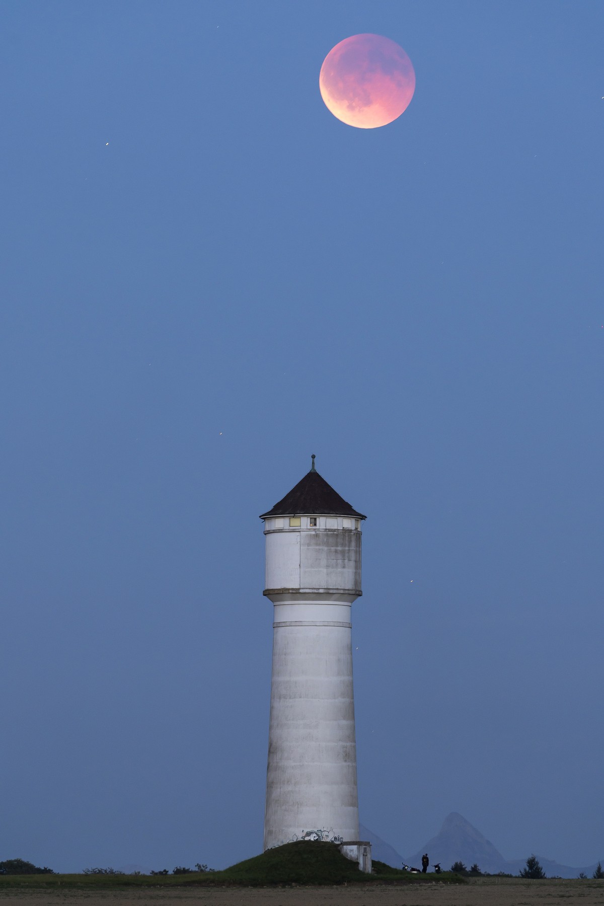 The lunar eclipse, blood moon, is pictured next to the water tower in Goumoens-la-Ville, Switzerland, Sunday, September 7, 2025 (KEYSTONE/Cyril Zingaro)