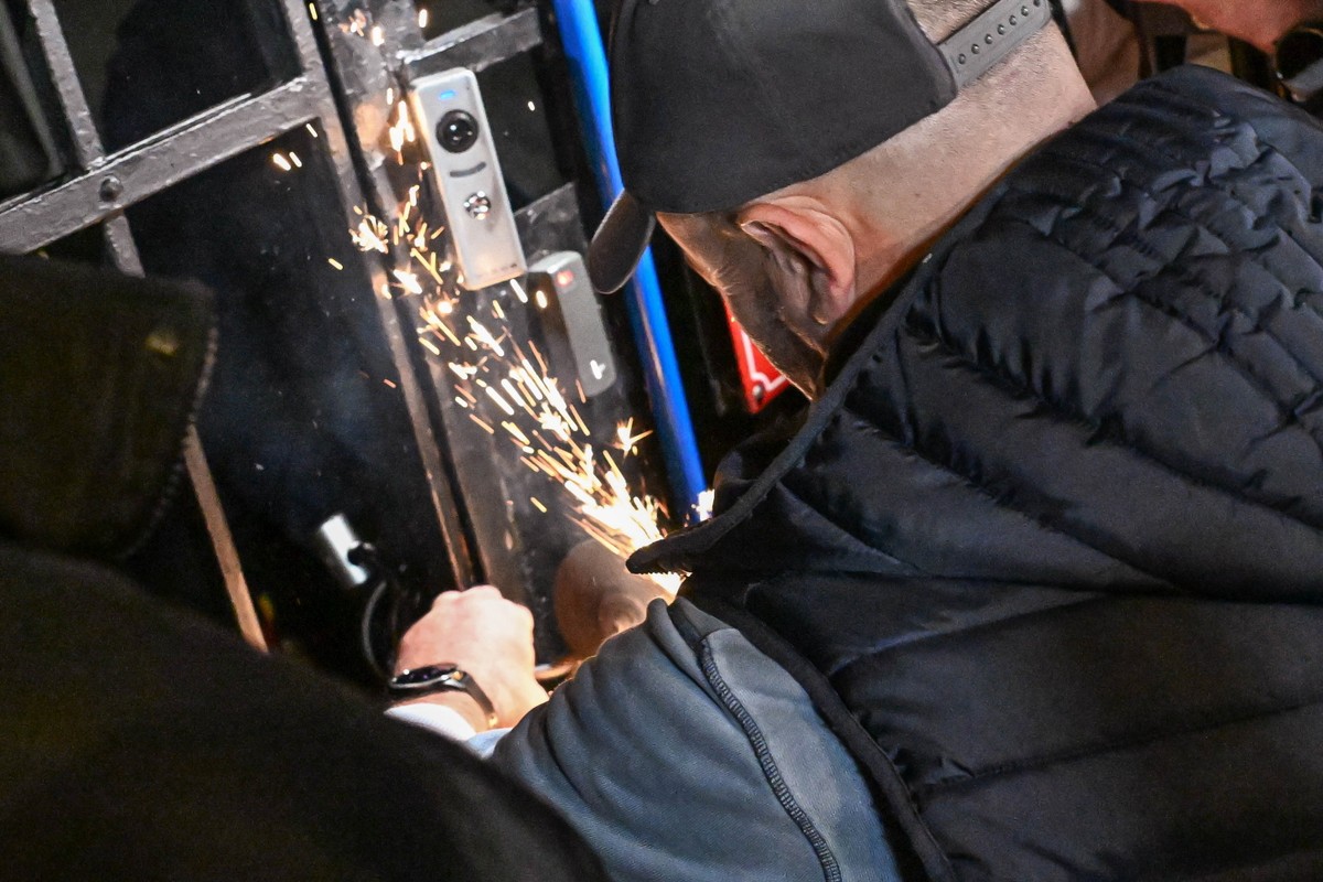 epa13342025 A man uses a saw to cut through a chain securing an entrance gate to the grounds of Poland's Constitutional Tribunal in Warsaw, Poland, 30 October 2026. The Warsaw Police Headquarters ...