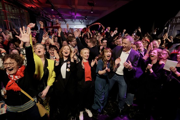 epa11919330 Heidi Reichinnek (C), top candidate for the Left Party (Die Linke), co-leaders Jan van Aken (C-R) and Ines Schwerdtner (C-L), react with party members to initial results during the party e ...