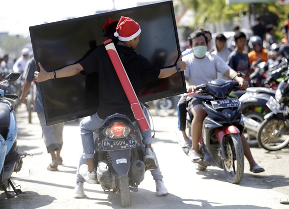 epa07058105 An Indonesian man carries a big screen TV looted from a tsunami devastated shopping mall in Palu, Central Sulawesi, Indonesia, 30 September 2018. According to reports, at least 384 people  ...