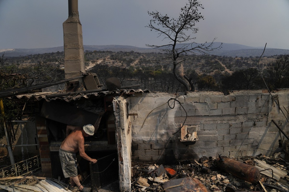 An owner of a burnt house try to clean after yesterday's fire in Mandra west of Athens, on Wednesday, July 19, 2023. Fast-moving wildfires swept across hills in the searing heat outside the Greek ...