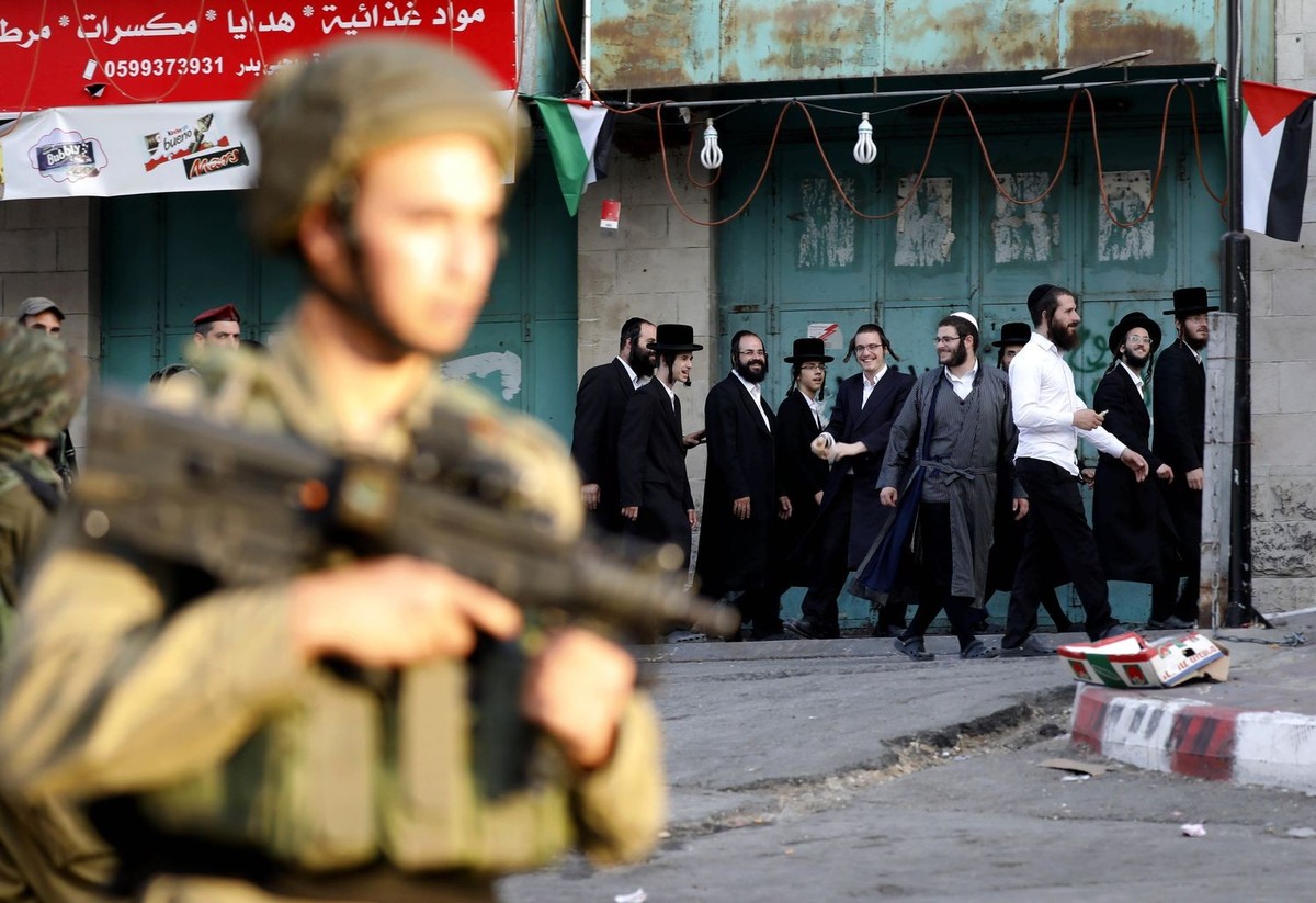 epa06120144 Israeli soldier stand guard while Ultra-Orthodox Jewish men under the protection of the soldiers visit a sacred Jewish site in the occupied West Bank city of Hebron, West Bank, 01 August 2 ...
