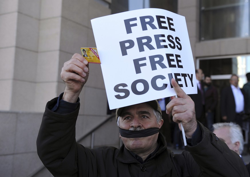 FILE - In this Friday, April 1, 2016 file photo, a Turkish journalist shows his press card as he covers his mouth with a black ribbon before the trial of Can Dundar, the editor-in-chief of opposition  ...