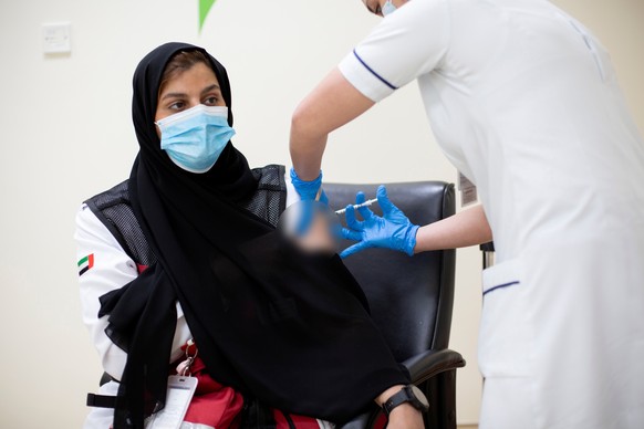 epa08900986 A handout photo made available by the Dubai Government of Media Office shows an Emirati employee of Dubai ambulance (L) receiving the first dose of the Pfizer-BioNTech COVID-19 vaccine in  ...
