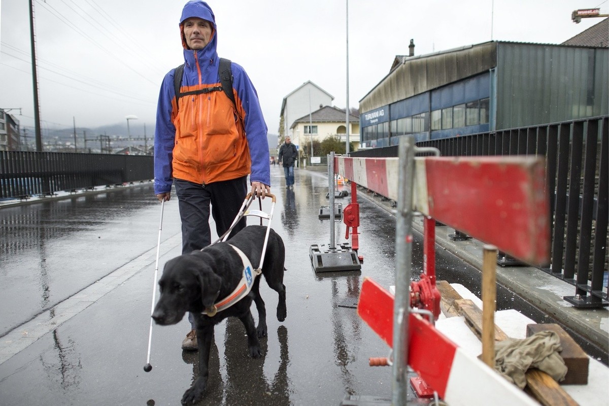 The nearly blind student Stephan Huesler, president of AGILE, with a white cane and his guide dog Dallas, passes a construction site on the way from Olten train station to the University of Applied Sc ...