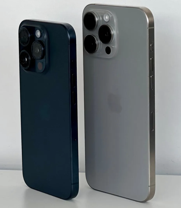 iPhone 15 Pro in Blau (links) und iPhone 15 Pro Max in Natur bei normalem Tageslicht. Das Blau wirkt oft sehr dunkel.