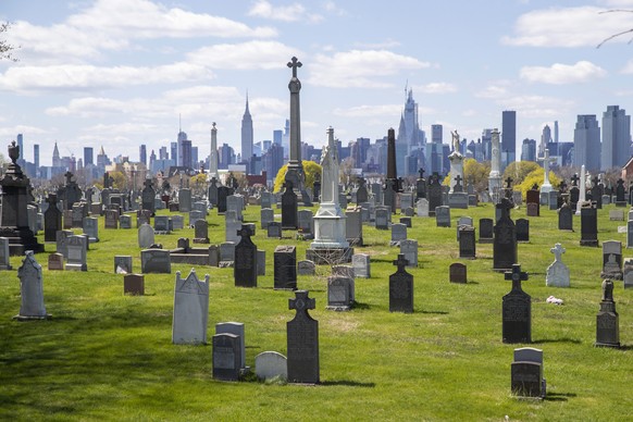 The Empire State building and the Manhattan skyline are seen behind the tombstones at Calvary Cemetery, Saturday, April 11, 2020, in the Maspeth neighborhood of the Queens borough of New York. The U.S ...