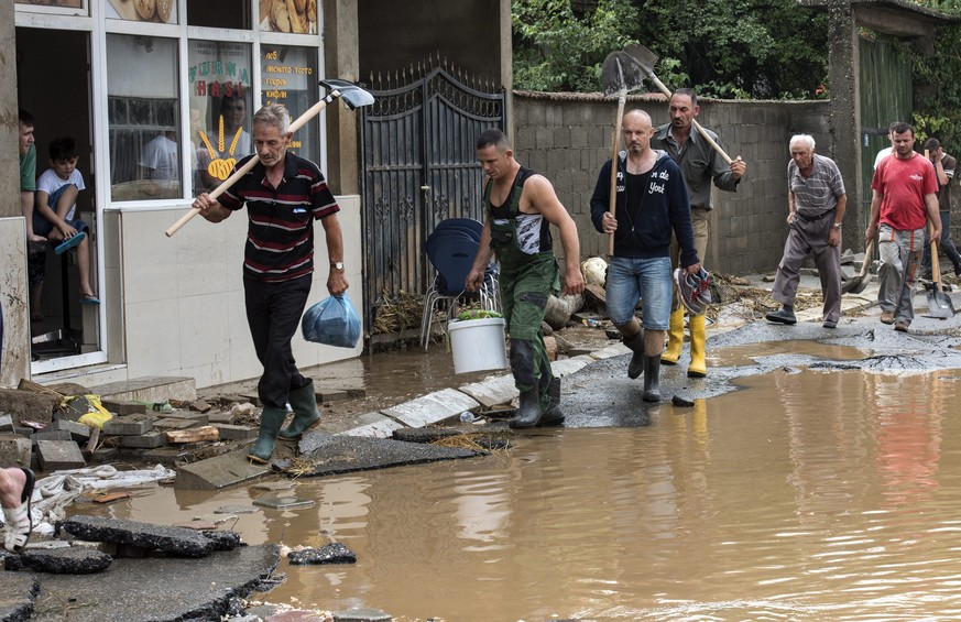 epa05461123 People with shovels walk through a flooded street in the village of Stajkovci, Skopje, The Former Yugoslav Republic of Macedonia on 07 August 2016. At least 15 people have died in a rain s ...