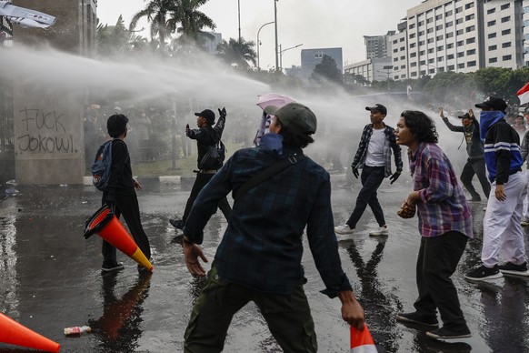 epa09884457 Students react as the police spray water as they clash during a protest outside the parliament building in Jakarta, Indonesia, 11 April 2022. Thousands of students in various regions in In ...