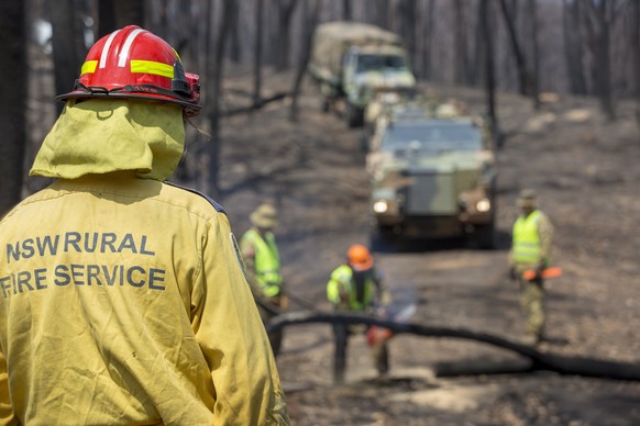 epa08119021 A handout photo made available by the Australian Department of Defence shows a New South Wales Rural Fire Service (NSW RFS) member watching on as Australian Army soliders conduct a route c ...