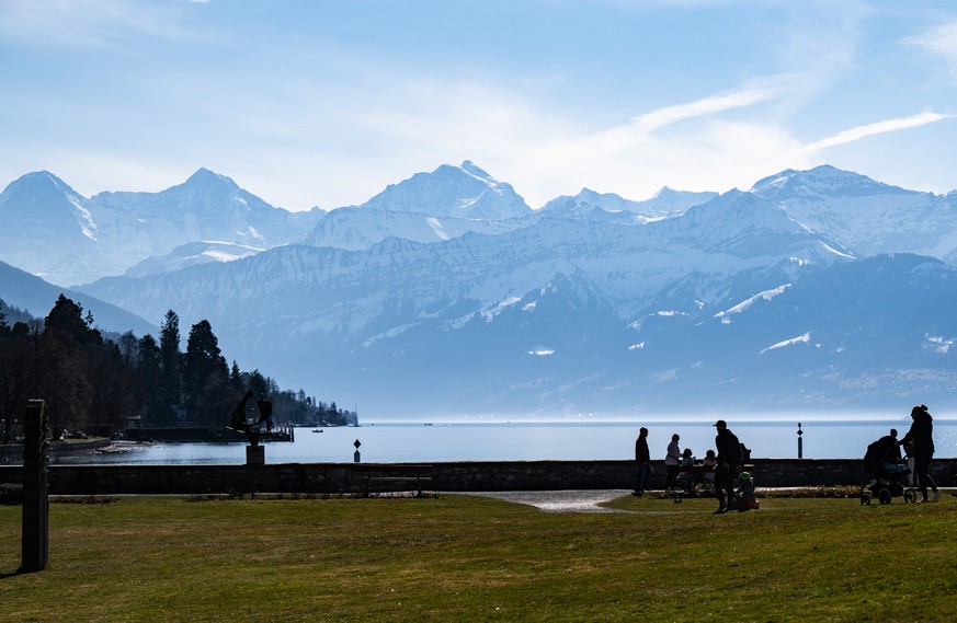 Personen spazieren mit Blick auf Eiger, Moench und Jungfrau im Schadaupark, am Sonntag, 13. Maerz 2022, in Thun. (KEYSTONE/Peter Schneider)