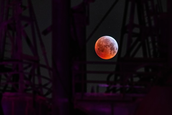 21.01.2019, Nordrhein-Westfalen, Duisburg: Als roter, sogenannter «Blutmond» praesentiert sich der Vollmond ueber einem angestrahlten Schornstein eines Hochofens im Landschaftspark Duisburg, waehrend  ...