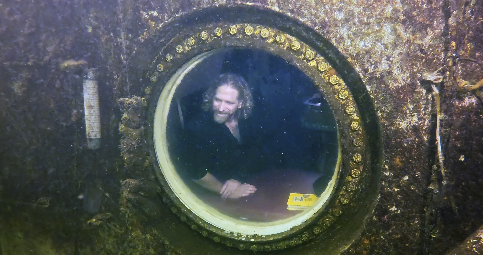 In this photo provided by the Florida Keys News Bureau, diving explorer and medical researcher Dr. Joseph Dituri peers out of a large porthole, Saturday, May 13, 2023, at Jules&#039; Undersea Lodge po ...
