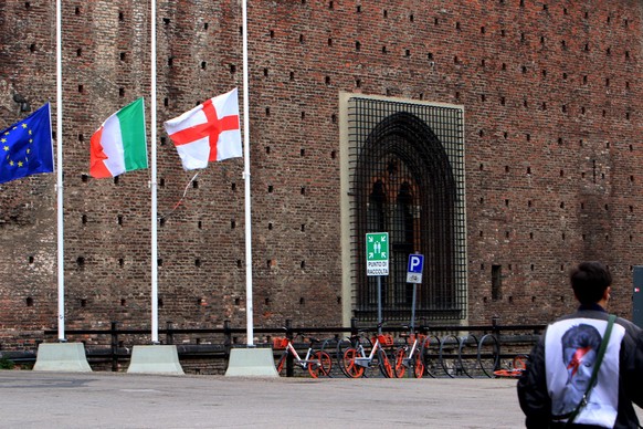 epa08334495 Flag of Europe, Italian flag and municipality of Milan flag are flown at half mast in Castello square, Milan, Italy, 31 March 2020. Flags are flown at half-mast across Italy as a minute of ...