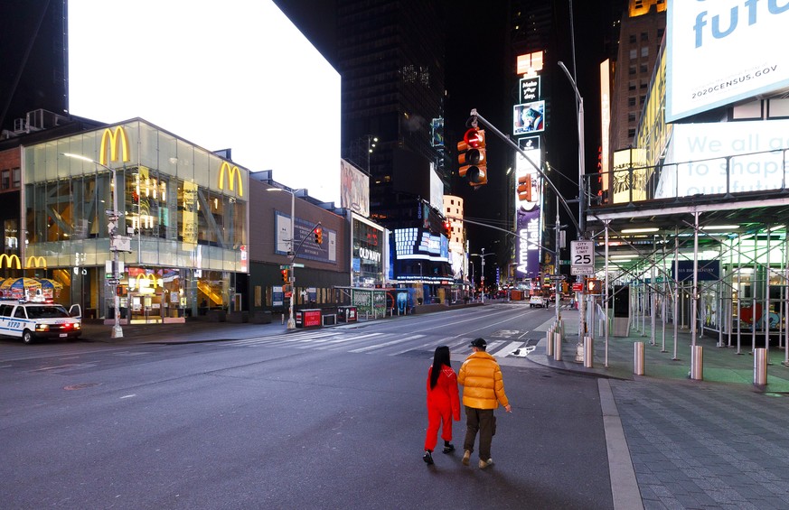 epaselect epa08323074 People walk through a nearly empty Times Square in New York, USA, 25 March 2020. A statewide shut down of all non-essential businesses and a ban on all non-solitary outside activ ...