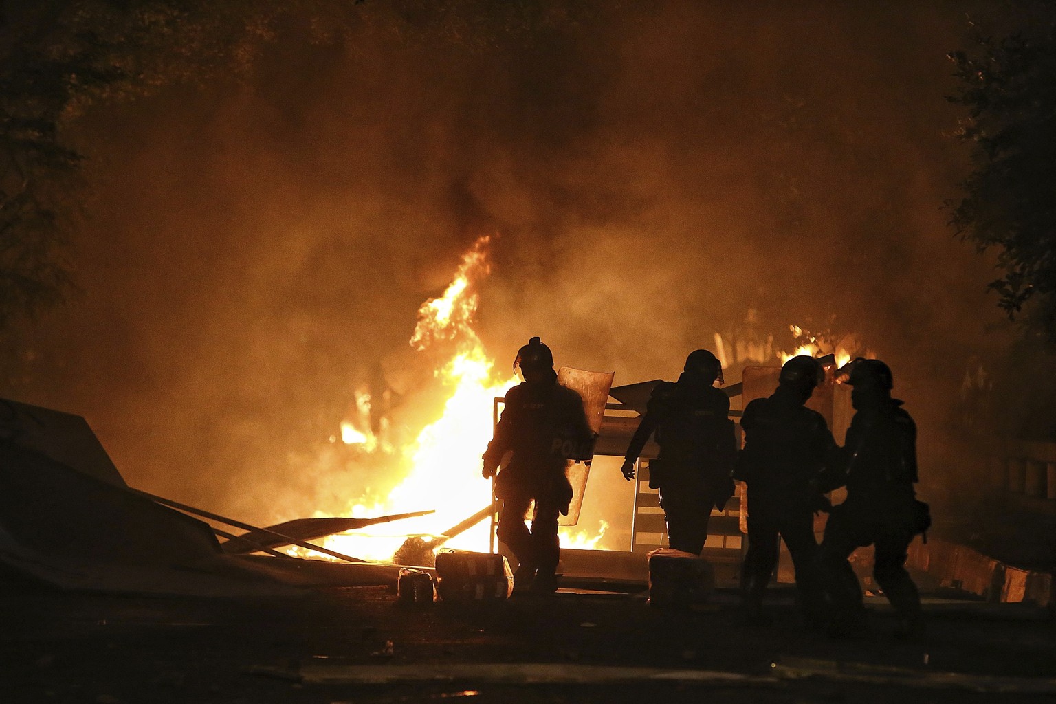 Riot police walk towards a burning barricade set up by protesters during a national strike to protest government-proposed tax reform, in Cali, Colombia, Friday, April 30, 2021. (AP Photo/Andres Gonzal ...