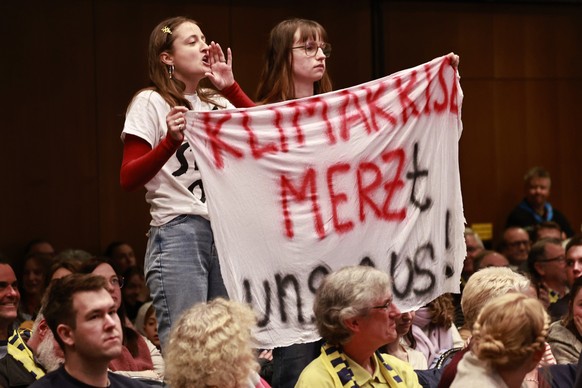 epa12959569 Activists hold a banner reading 'the climate destroys us' as they protest during a talk with youth and German Chancellor Friedrich Merz at the 104th German Catholic Convention (K ...