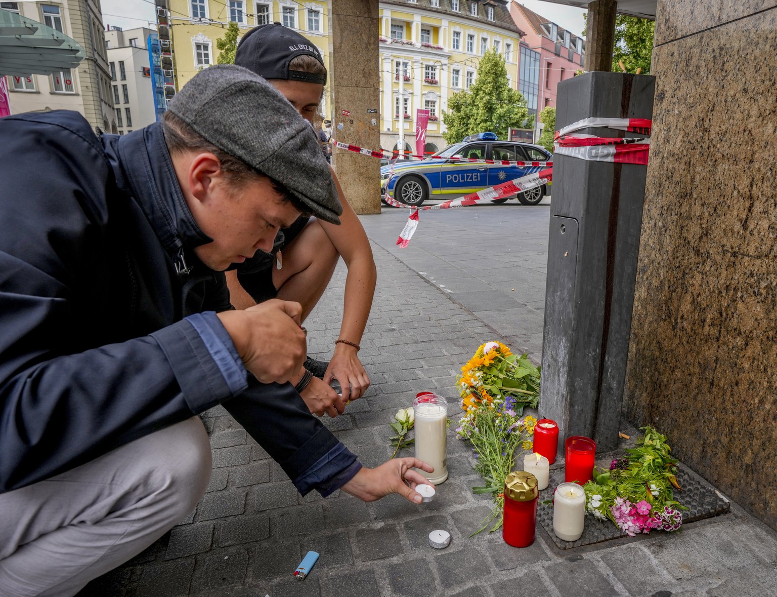 Flowers and candles are laid by young men at the crime scene in central Wuerzburg, Germany, Saturday, June 26, 2021. German police say several people have been killed and others injured in a knife att ...