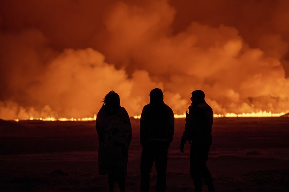 People watch as the night sky is illuminated caused by the eruption of a volcano in Grindavik on Iceland&#039;s Reykjanes Peninsula, Monday, Dec. 18, 2023. (AP Photo/Marco Di Marco)