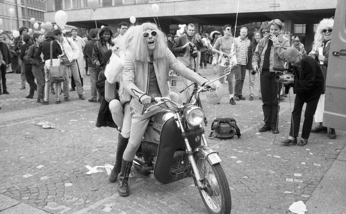 "Christopher Street Day, Zürich, 24.06.1995", Helvetiaplatz - Mann in Frauenkleidung und eine weitere Person auf einem Motorrad; rundherum versammelte Teilnehmende