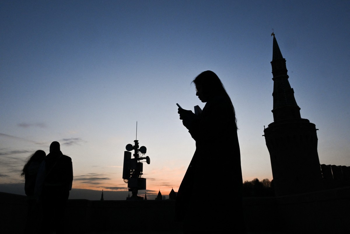 A woman uses her smartphone as she walks on the Moskvoretsky bridge past a cell tower in central Moscow on March 17, 2026. (Photo by Igor IVANKO / AFP)