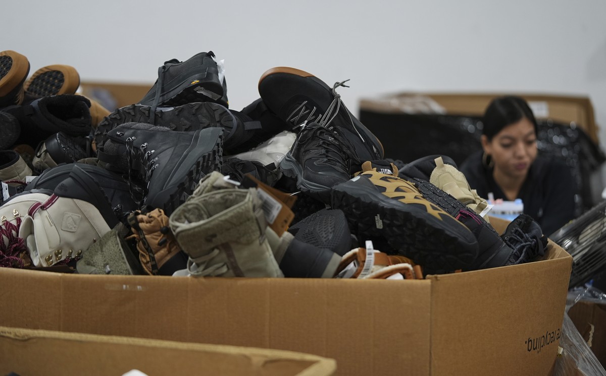 People work amid boxes of returned or overstocked clothing, shoes, boots, coats, packs and other items in a warehouse where the goods are cleaned or repaired before they are marketed on resale platfor ...