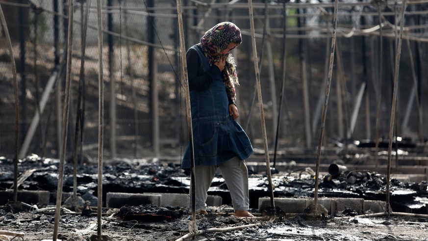 A migrant stands among the remains of a burned tent at the Moria migrant camp, after a fire that ripped through tents and destroyed containers during violence among residents, on the island of Lesbos, ...