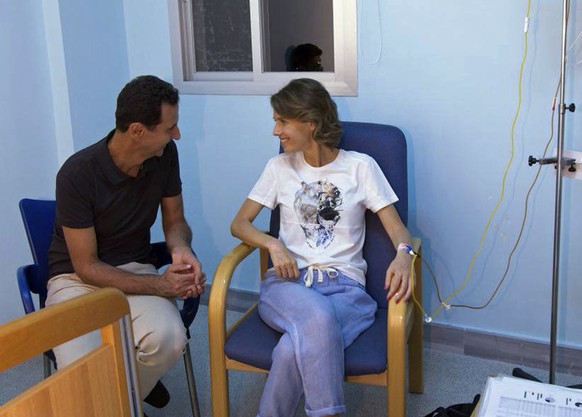 This photo posted Wednesday, Aug 8, 2018 on the official Facebook page of the Syrian Presidency, shows Syrian President Bashar Assad sitting next to his wife Asma Assad with an IV in her left arm in w ...