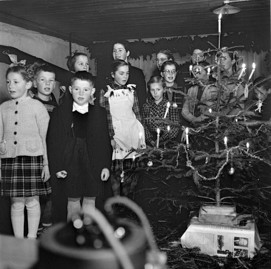 Kinder singen, um den Christbaum versammelt, im Schulzimmer in Ablaendschen, Kanton Bern. Aufgenommen im Dezember 1951. (KEYSTONE/PHOTOPRESS-ARCHIV/Margrit Baeumlin)