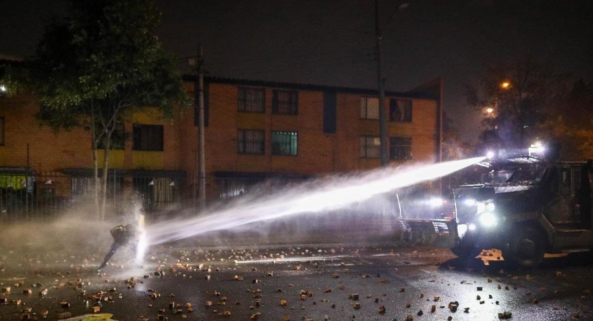 This viral photograph captures a lone protester blocking a powerful stream of water from an ESMAD riot police water cannon truck using an improvised metal shield during the 2021 national protests in C ...