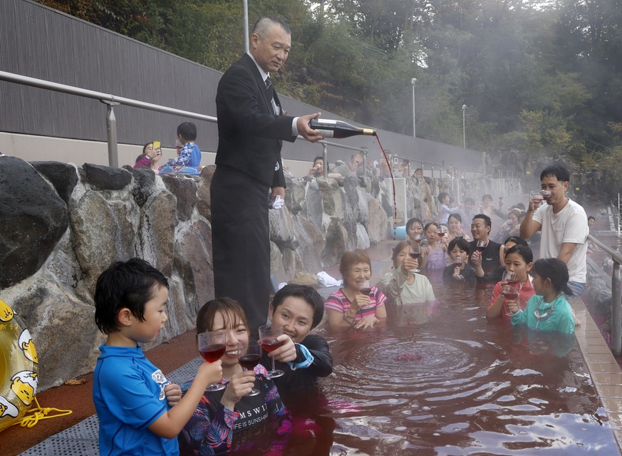 epa11732341 A sommelier pours 2024 Beaujolais Nouveau wine as people bathe in a red-colored hot water bath on the day of the Beaujolais Nouveau official release at Hakone Kowakien Yunessun hot spring  ...