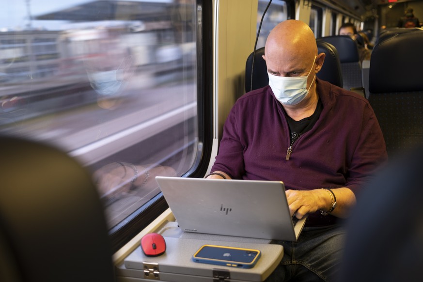 epa09091961 Passenger wearing protective mask works on a laptop as he rides a Swiss Federal Railways SBB CFF FFS train during the coronavirus disease (COVID-19) outbreak, in Neuchatel, Switzerland, 23 ...