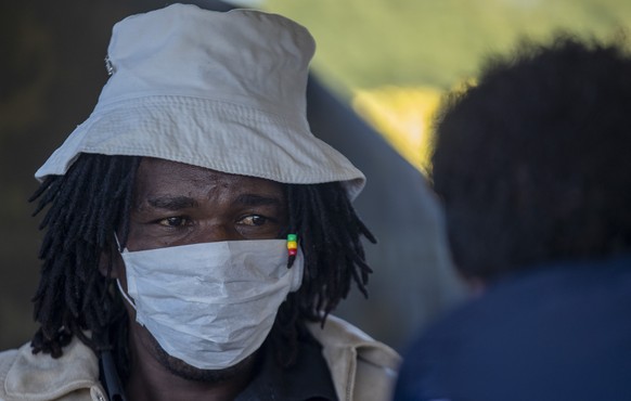 A man wearing a face mask looks on as the health worker screens and to be tested for COVID-19 at Lenasia South Hospital, south Johannesburg, South Africa, Tuesday, April 21, 2020, during a campaign ai ...