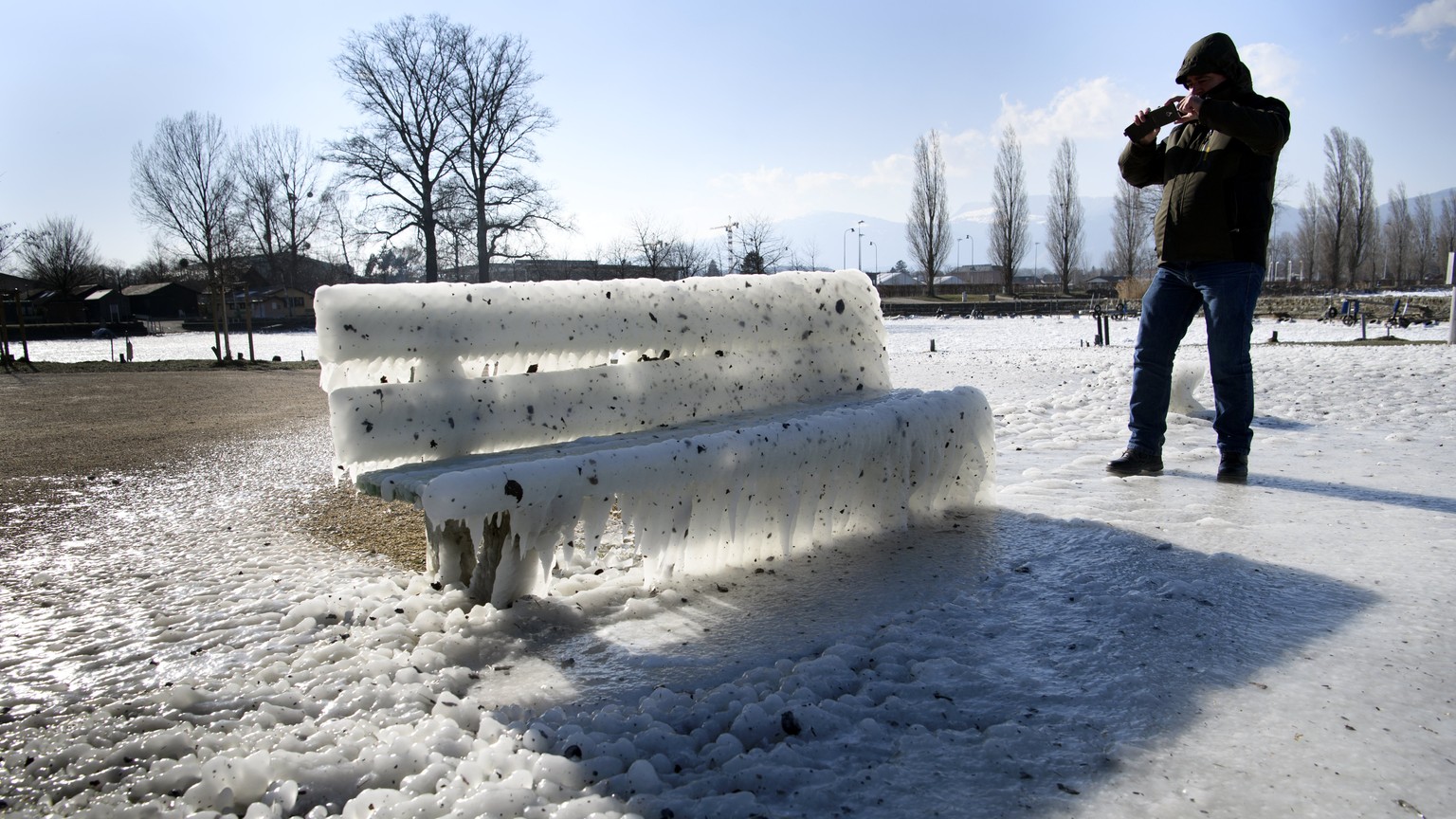 epa06566838 A man takes picture of ice-covered bench on the frozen shores of the Lake of Neuchatel, in Yverdon-les-Bains, Switzerland, 26 February 2018. Media reports on 26 February state that extreme ...