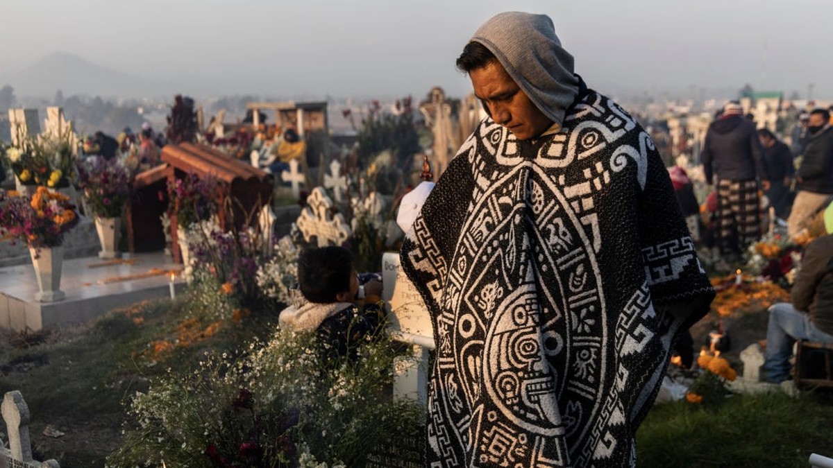 SAN PABLO AUTOPAN, MEXICO - NOVEMBER 2: A man stands in front of the grave of his relatives during sunrise at the San Pablo Autopan cemetery during sunrise at the San Pablo Autopan cemetery during   ...