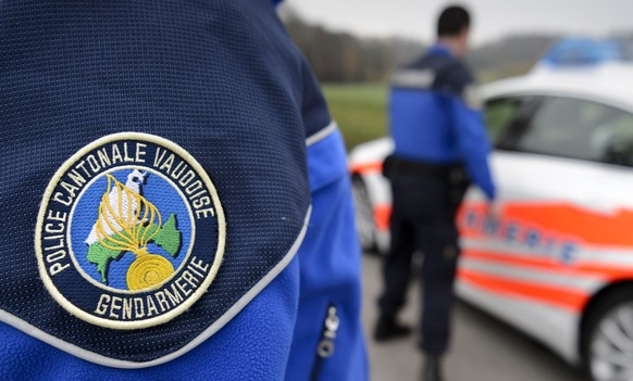 [Editor's note: photo mise-en-scene] Detail view of the uniform of a police officer of the cantonal police of Vaud, in the foreground, and another cantonal police officer next to a police car, in ...