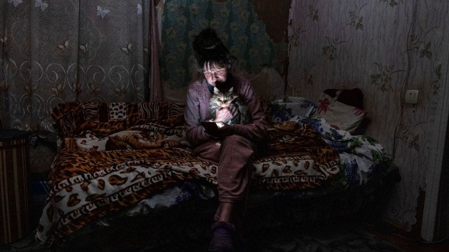 Tetyana Safonova sits on the bed with her cat during a power outage, Borodyanka, October 20, 2022.