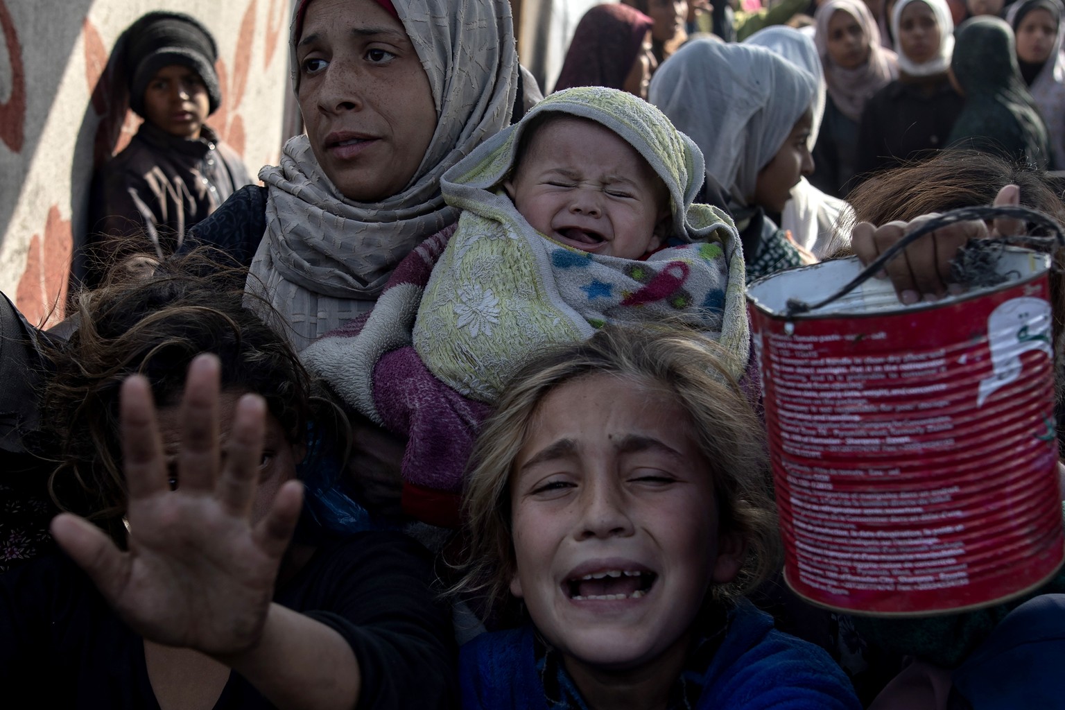 epa11816531 Palestinians, including children, hold metal pots and pans as they gather to receive food cooked by a charity kitchen, in Khan Yunis, southern Gaza Strip, 10 January 2025. According to the ...