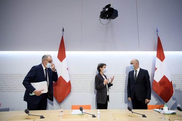 Bundespraesidentin Simonetta Sommaruga, Mitte, und Bundesrat Alain Berset, rechts, sprechen an der Seite von Bundesrat Guy Parmelin, links, nach einer Medienkonferenz, am Freitag, 18. Dezember 2020, i ...