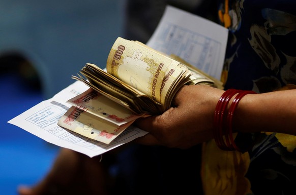 A woman holds 500 and 1000 Indian rupee banknotes as she stands in a queue to deposit her money inside a bank in the northern city of Kanpur, India, November 10, 2016. REUTERS/Adnan Abidi