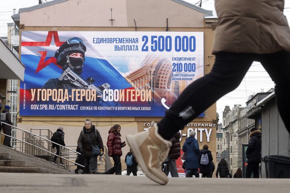 epa11918236 People walk past a digital billboard showing an advertisement for military service with the slogan &#039;A heroic city has its heroes&#039; during the &#039;Defender of the Fatherland Day& ...