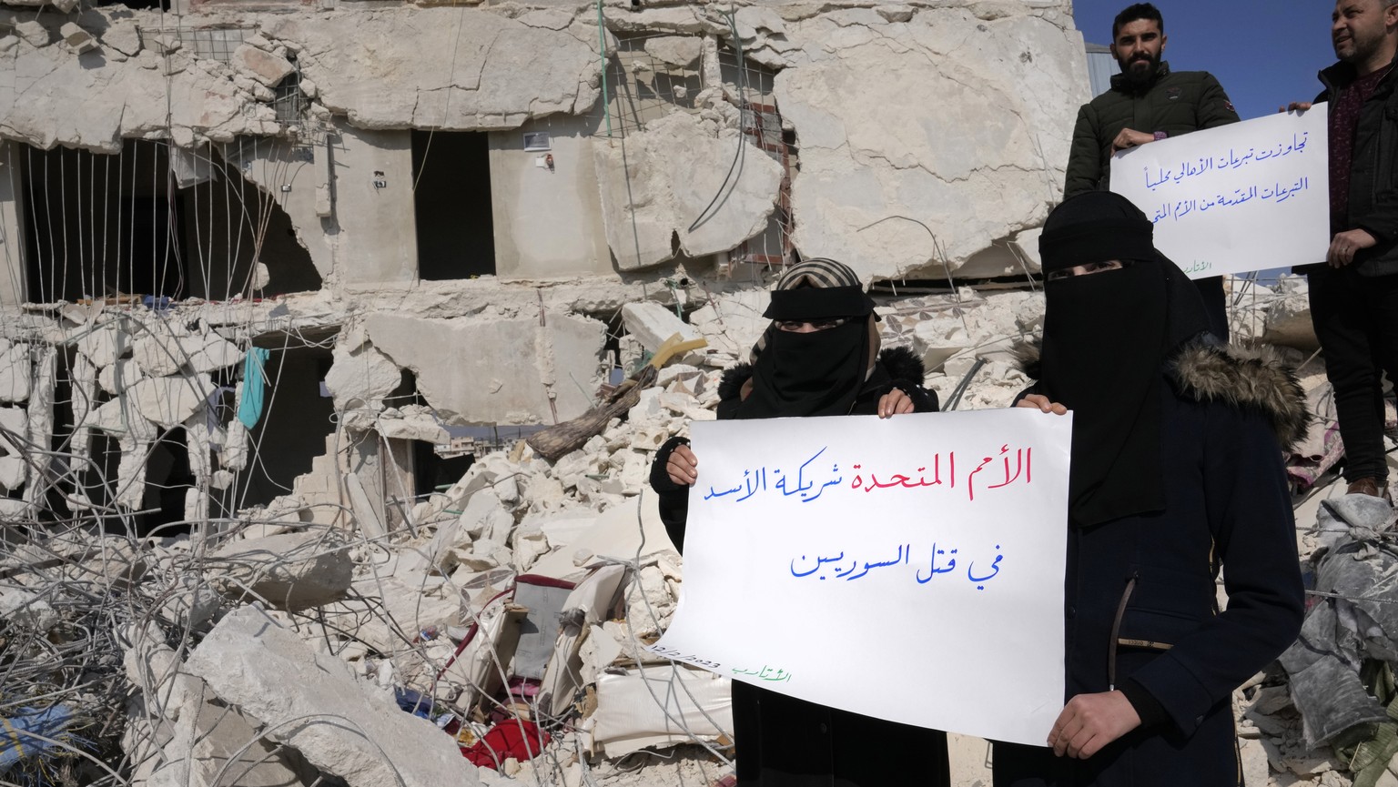 FILE - Women stand amidst the rubble of destroyed houses with placards in Arabic reading &quot;United Nations are the partners of Bashar Assad and killing Syrians,&quot; in Atareb, Syria, Sunday, Feb. ...