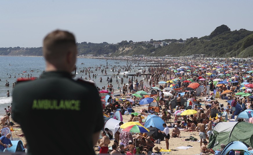 A member of the Ambulance service looks out at people crowded on the beach in Bournemouth, England, Thursday June 25, 2020, as coronavirus lockdown restrictions have been relaxed. According to weather ...