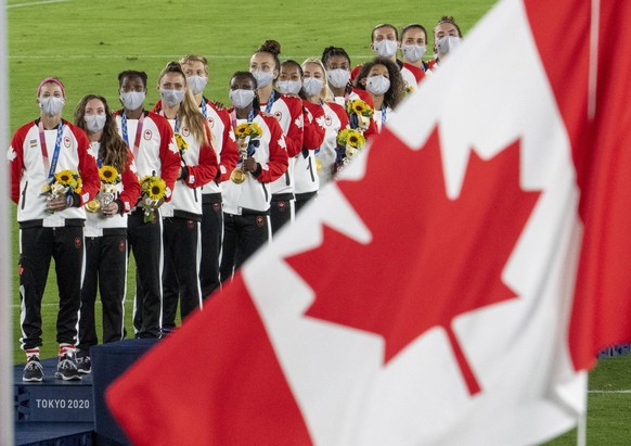 August 6, 2021, Tokyo, JAPAN: Members of the Canadian women��� s soccer team watch the flag raise after being presented with their gold medals at the Tokyo Olympics in Tokyo, Japan on Friday August 6, ...