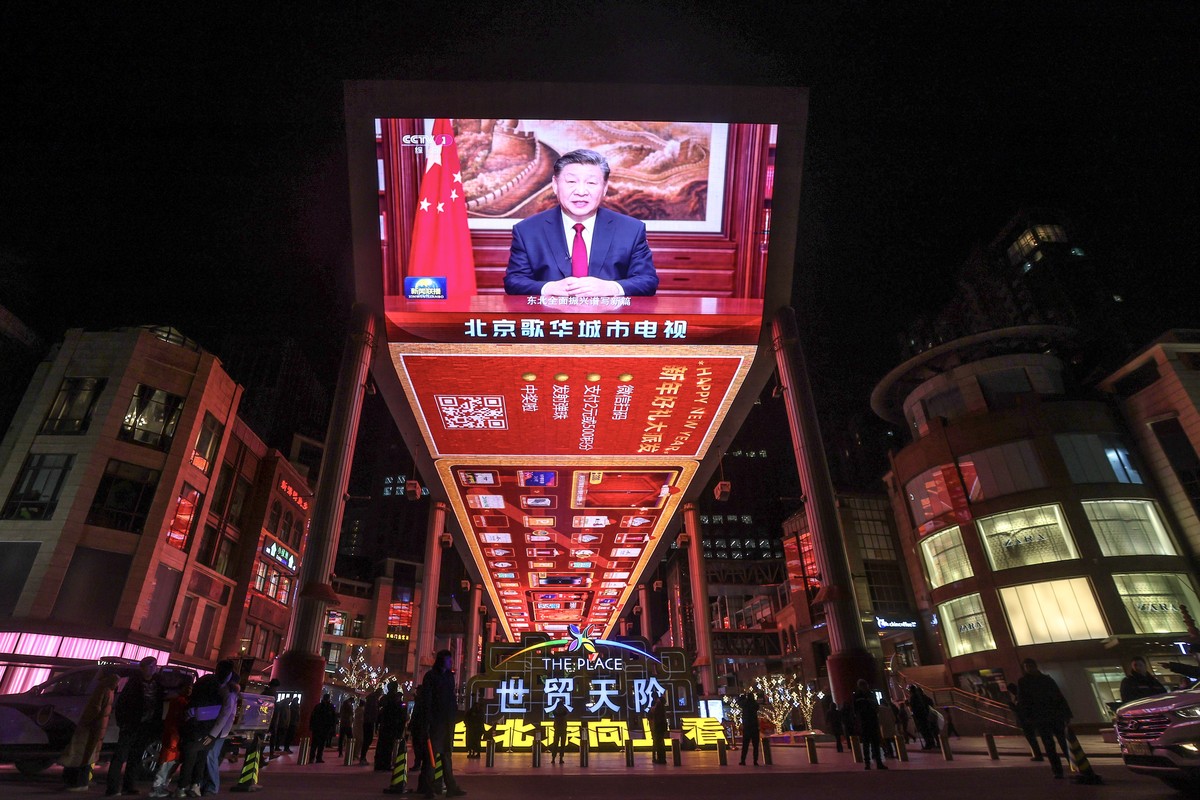 epaselect epa11050285 People walk past a screen that shows Chinese President Xi Jinping delivering a New Year address to ring in 2024, in Beijing, China, 31 December 2023. EPA/WU HAO