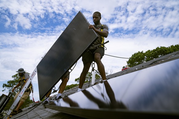 FILE - Employees of NY State Solar, a residential and commercial photovoltaic systems company, install an array of solar panels on a roof, Aug. 11, 2022, in the Long Island hamlet of Massapequa, N.Y.  ...