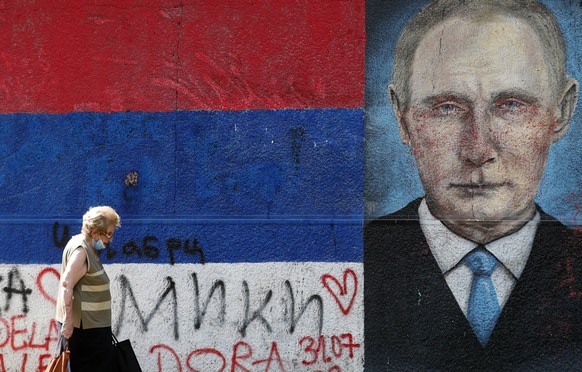 A woman wearing a mask to protect against the spread of coronavirus passes by graffiti depicting Russian President Vladimir Putin in Belgrade, Serbia, Wednesday, Aug. 19, 2020. Putin says that a coron ...