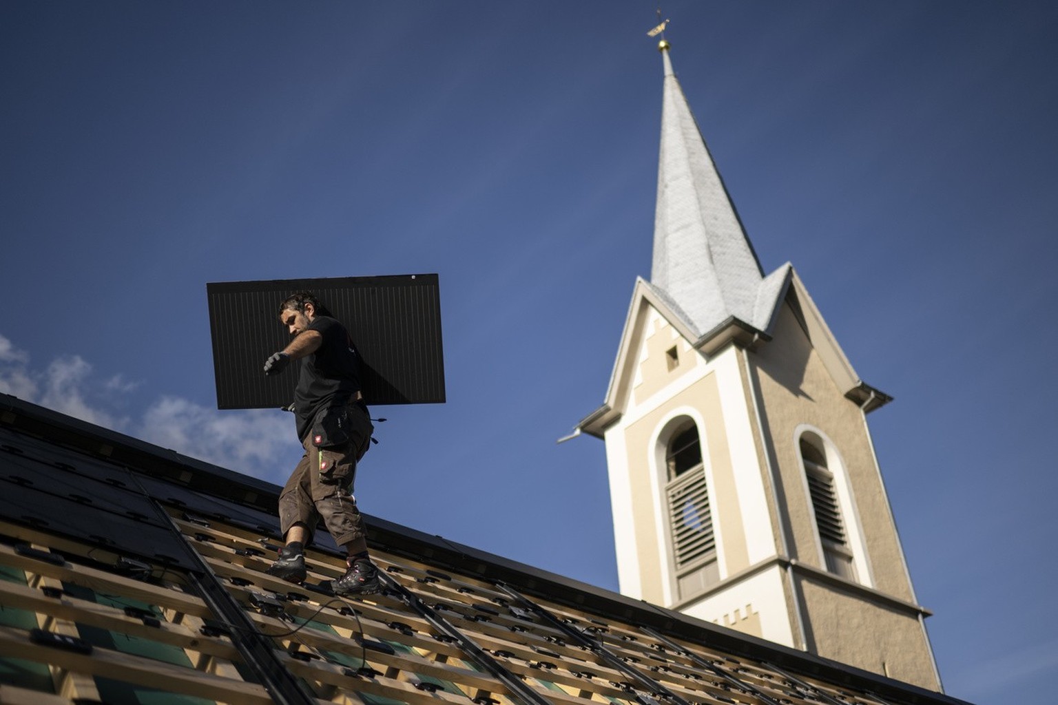 Arbeiter Simon Wettstein montiert Solarpanels auf dem Dach der historischenKirche, aufgenommen am Dienstag, 19. September 2023, in Trin. (KEYSTONE/Gian Ehrenzeller)