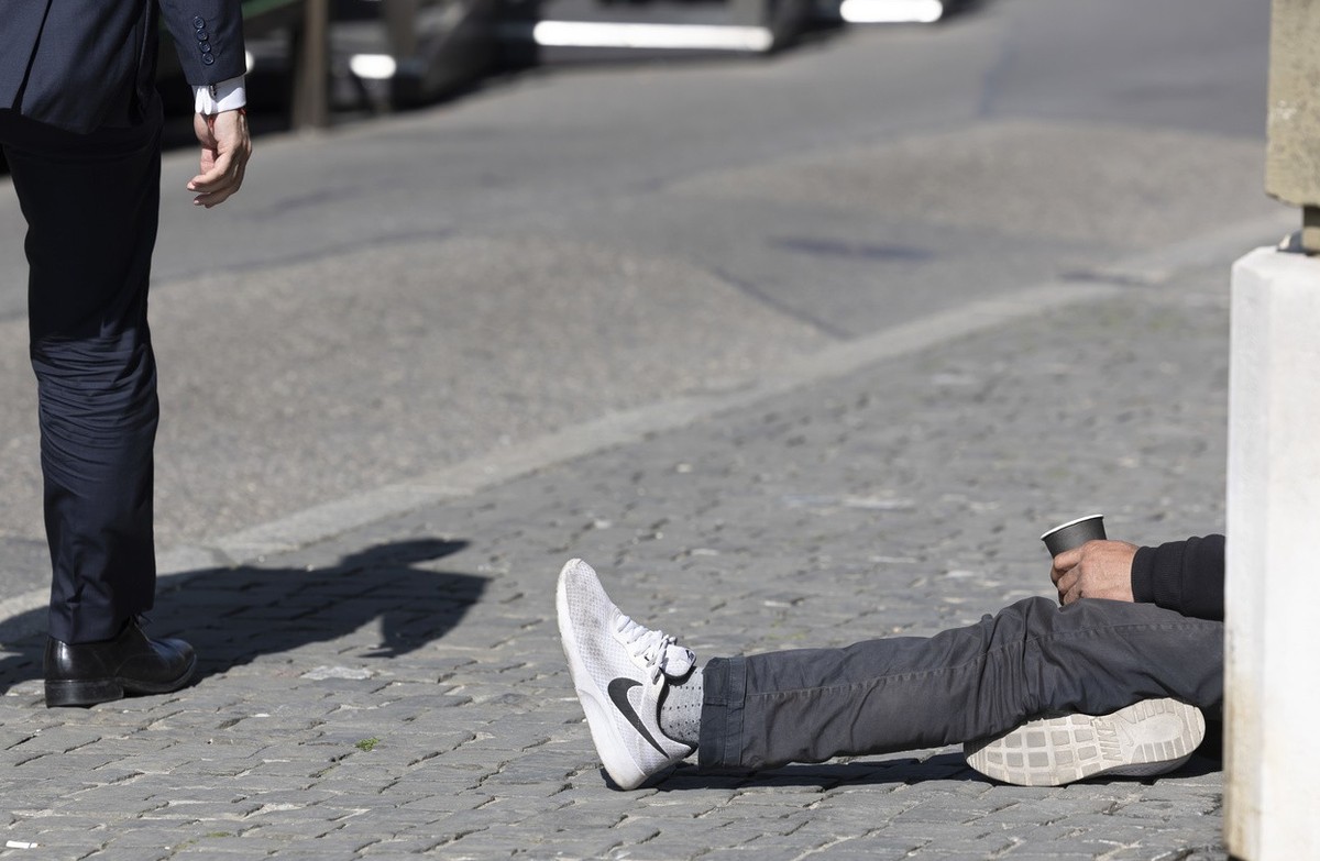 Un homme passe vers un mendiant qui fait la manche sur la place du Bourg-de-Fourg, ce vendredi 25 mars 2022 a Geneve. (KEYSTONE/Salvatore Di Nolfi)
